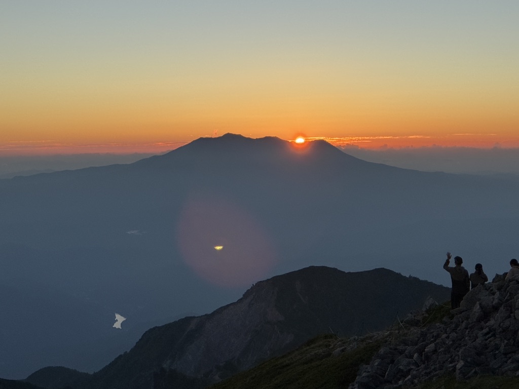 御嶽山の上に沈む夕日と、稜線でそれを見送る登山者のシルエット
