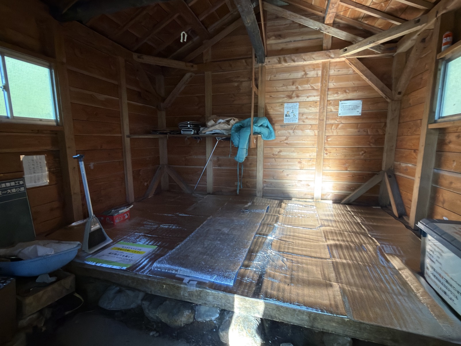 大樽避難小屋の内部。板の間に銀マットが敷かれ荷物棚がある