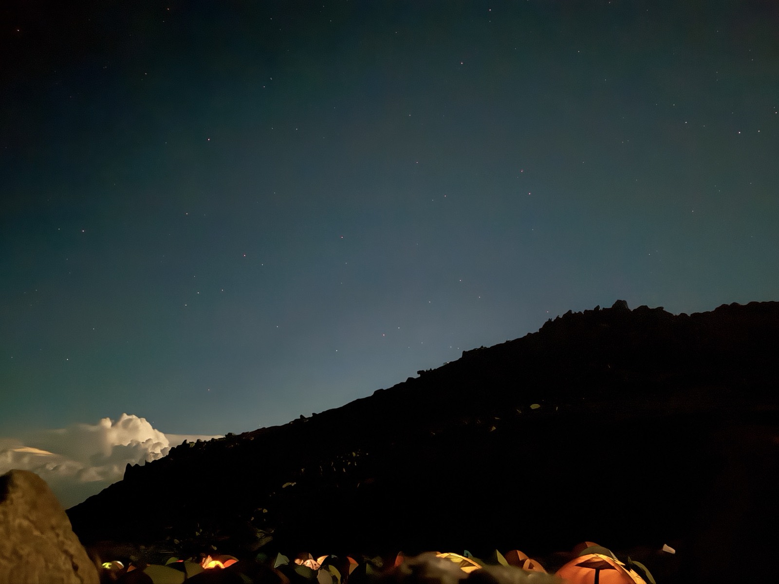 夜の稜線のシルエットとテントの灯り、星空
