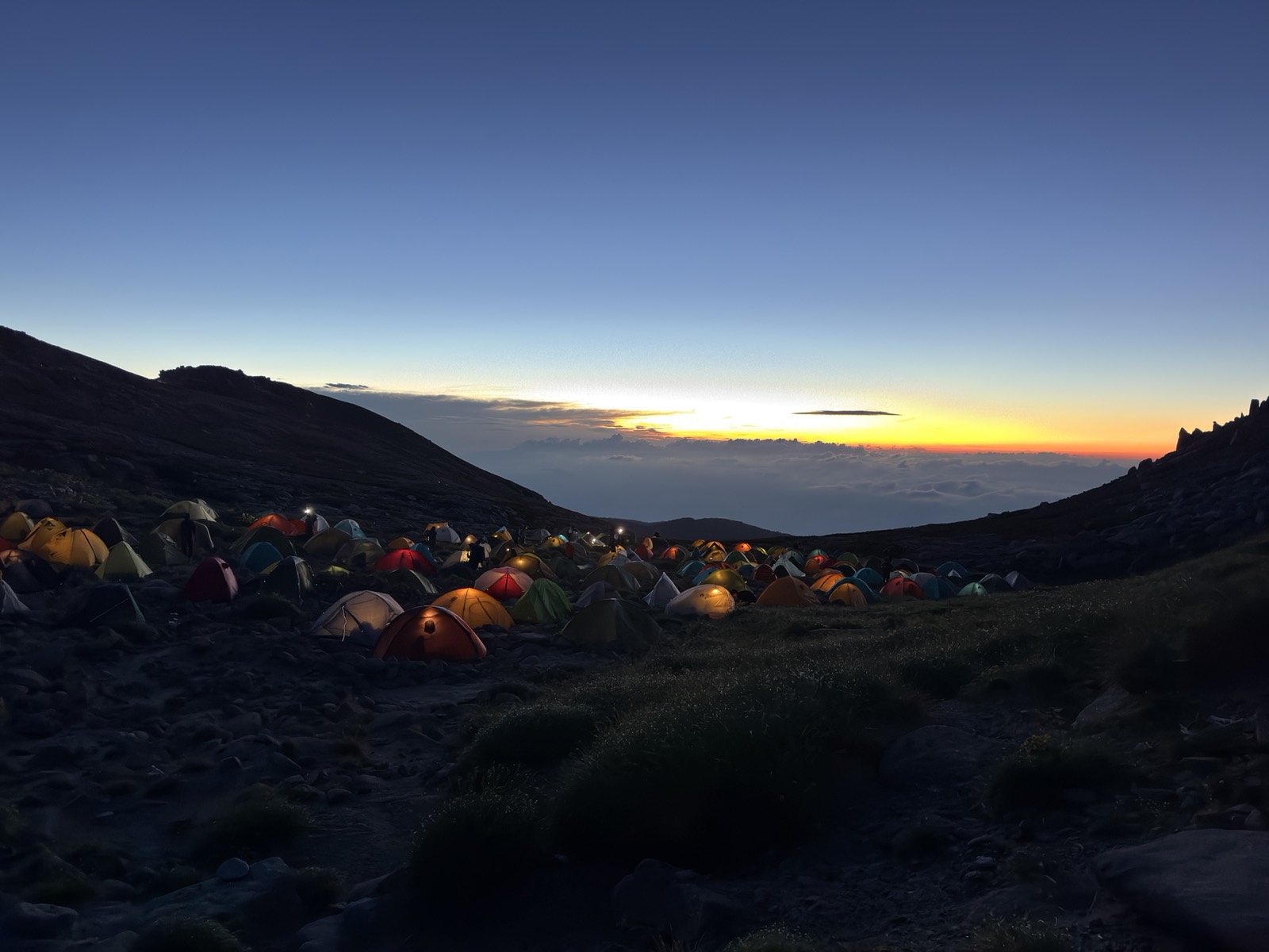 夜明け前のテント場。テントの灯りと朝焼けが始まる地平線