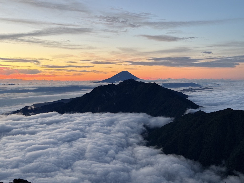 甲斐駒ヶ岳の山頂から見た夜明け前の空。雲海の向こうに富士山と鳳凰三山のシルエット