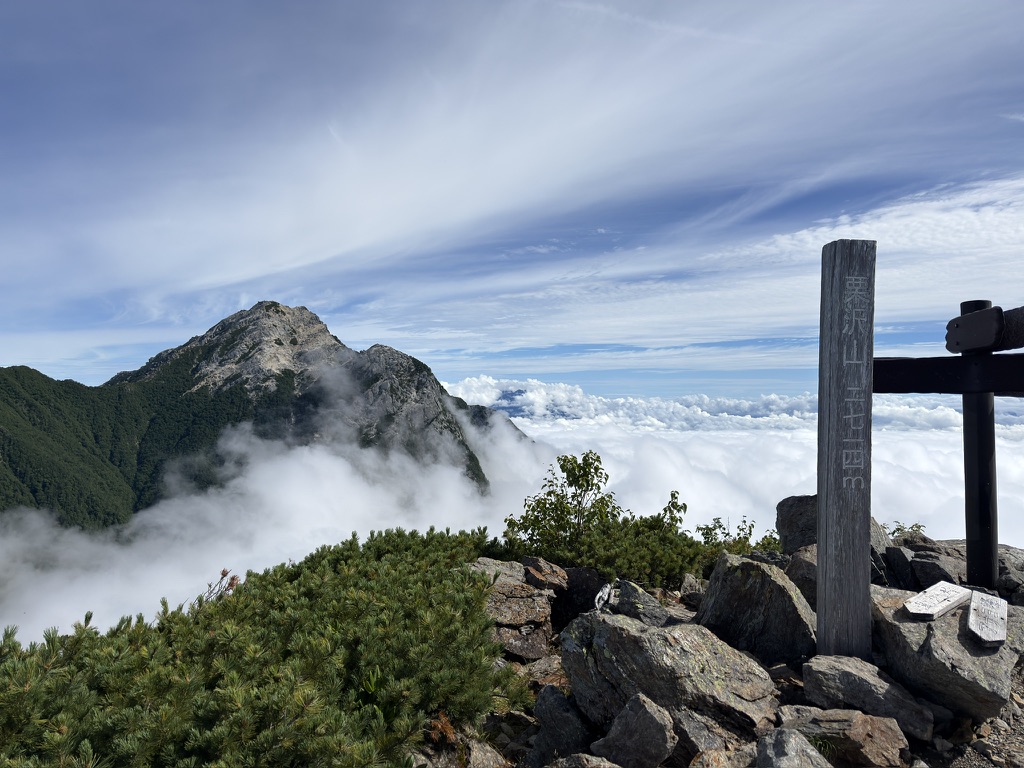 栗沢山の山頂標識「栗沢山 2714M」と、その奥の甲斐駒ヶ岳