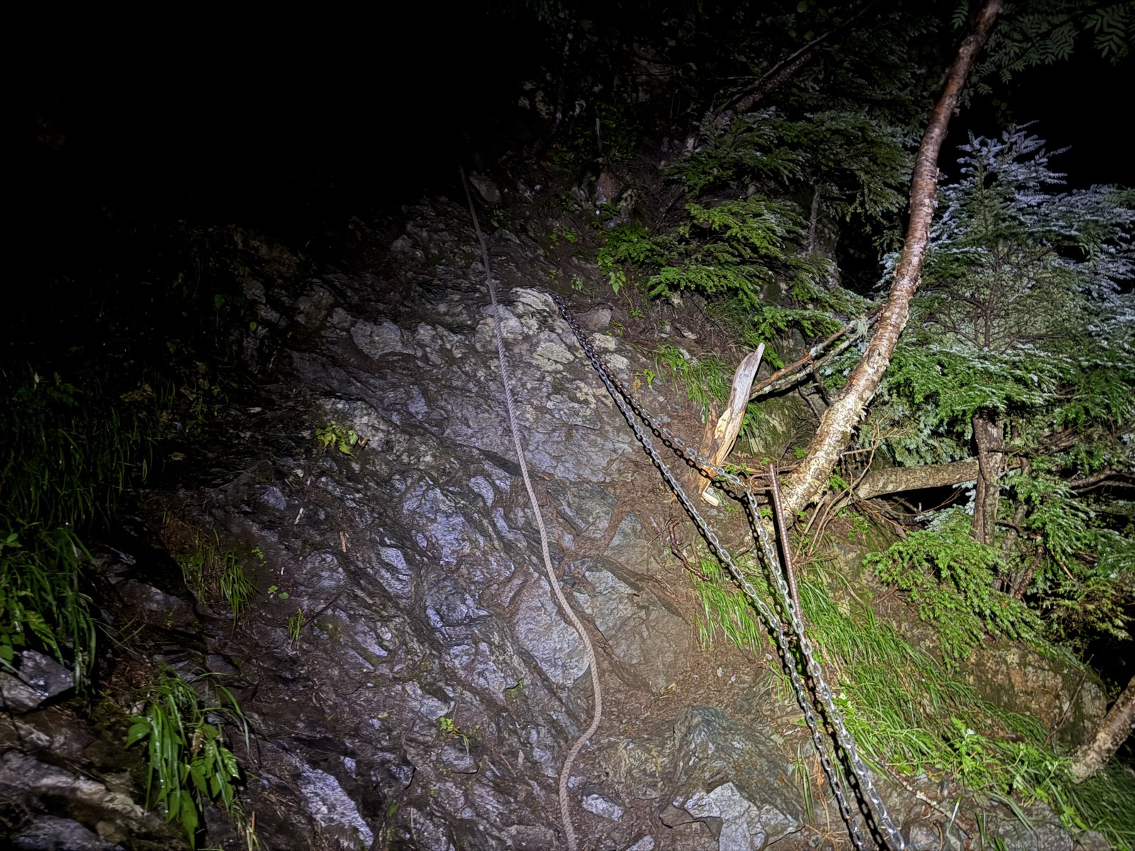 夜の鎖場。濡れた岩に鎖とロープ