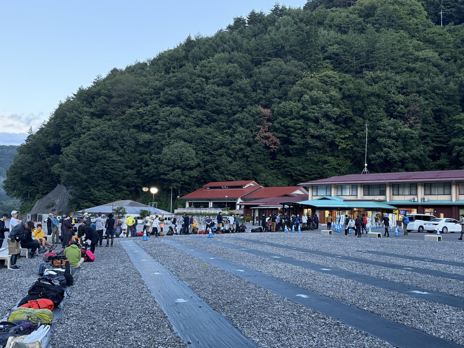 夜明けの戸台パーク全景。黒シートのレーンが3本、その脇にザックが並ぶ。奥に仙流荘