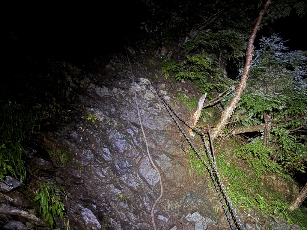 ヘッドランプの光に照らされた、夜の岩場と鎖