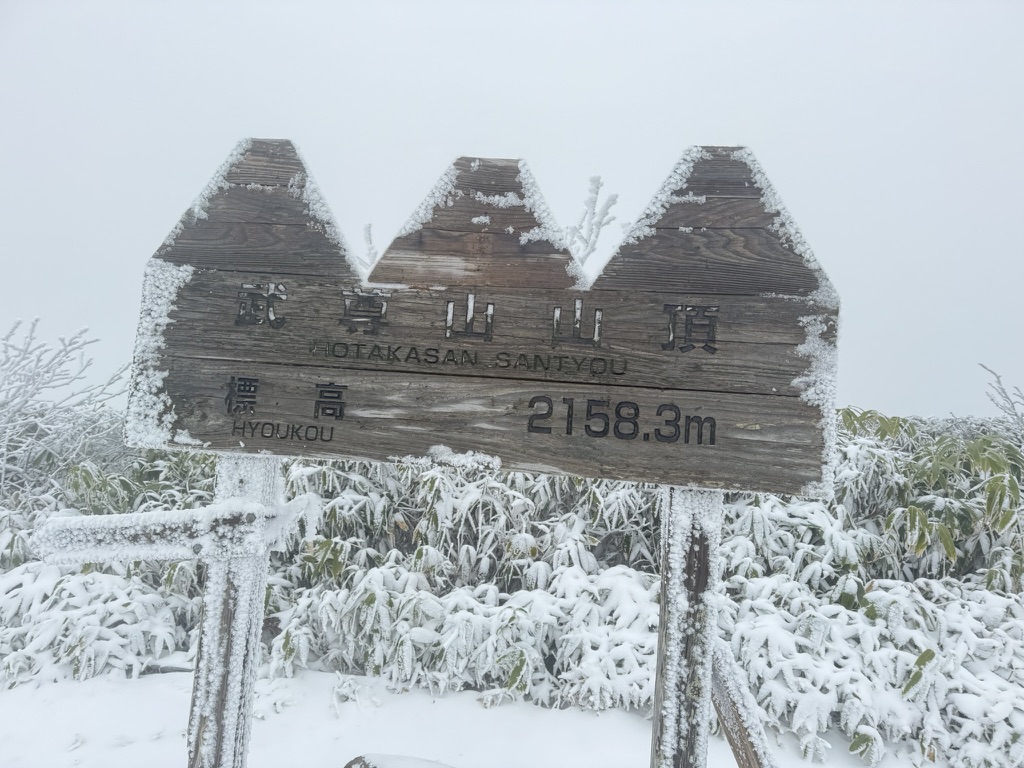 雪をかぶった武尊山の山頂標識。標高2158.3mの表示