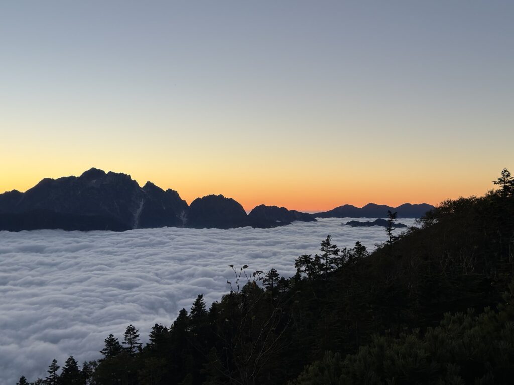 日没後の茜色の空と剱岳のシルエット、手前に広がる雲海