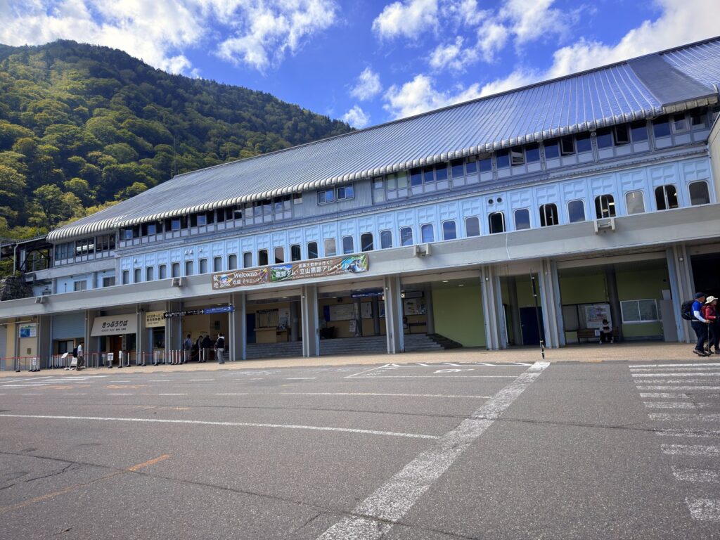 昼間の扇沢駅の駅舎と駅前の駐車場