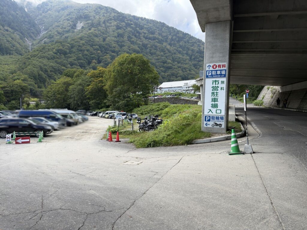 扇沢の道路沿いの案内看板。有料駐車場は直進、無料の市営駐車場入口と駐輪場