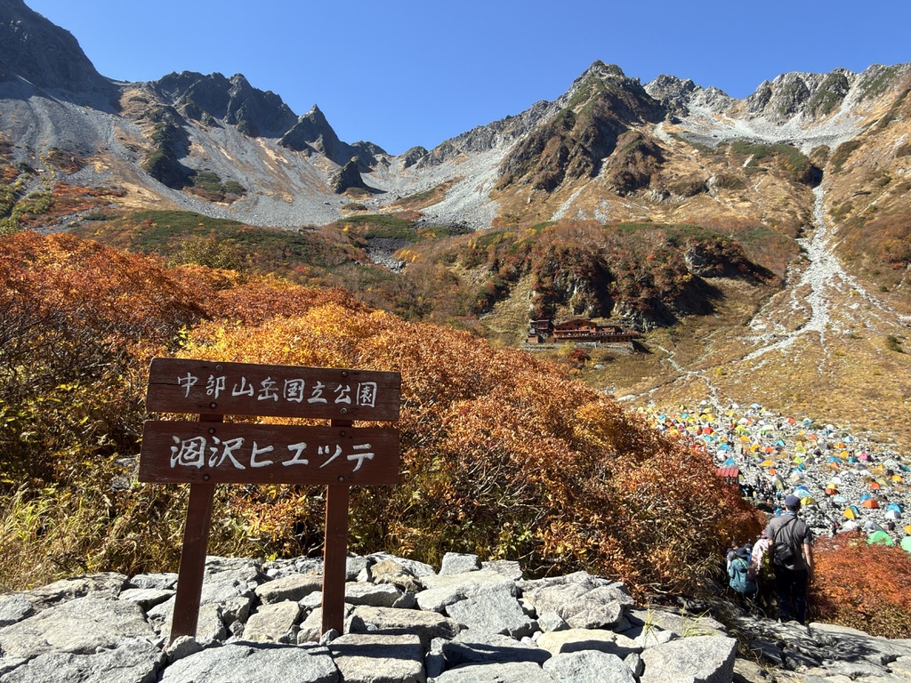 涸沢ヒュッテの看板。紅葉の向こうに涸沢小屋とテント場